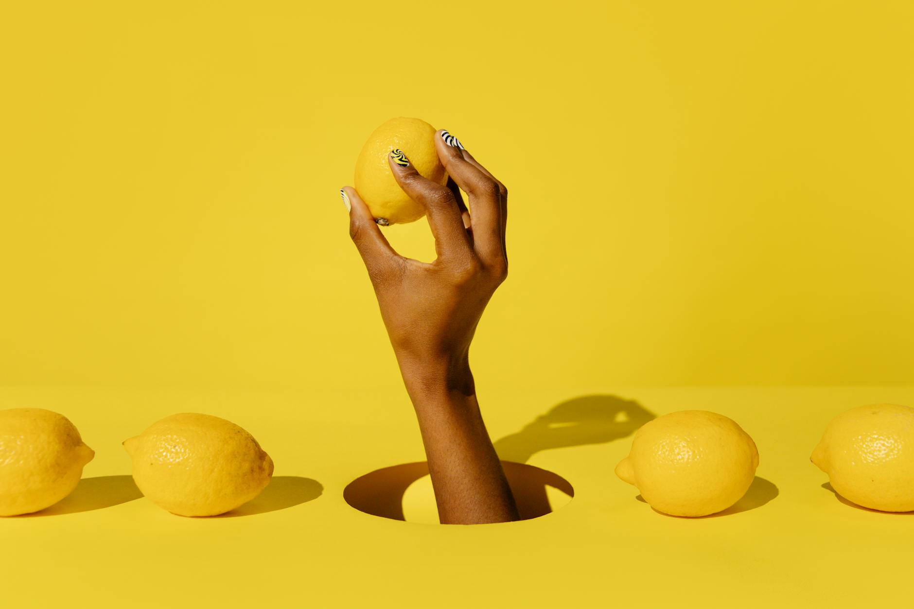 A hand holding a fresh lemon against a vivid yellow background, symbolizing bright, uncomplicated pleasure