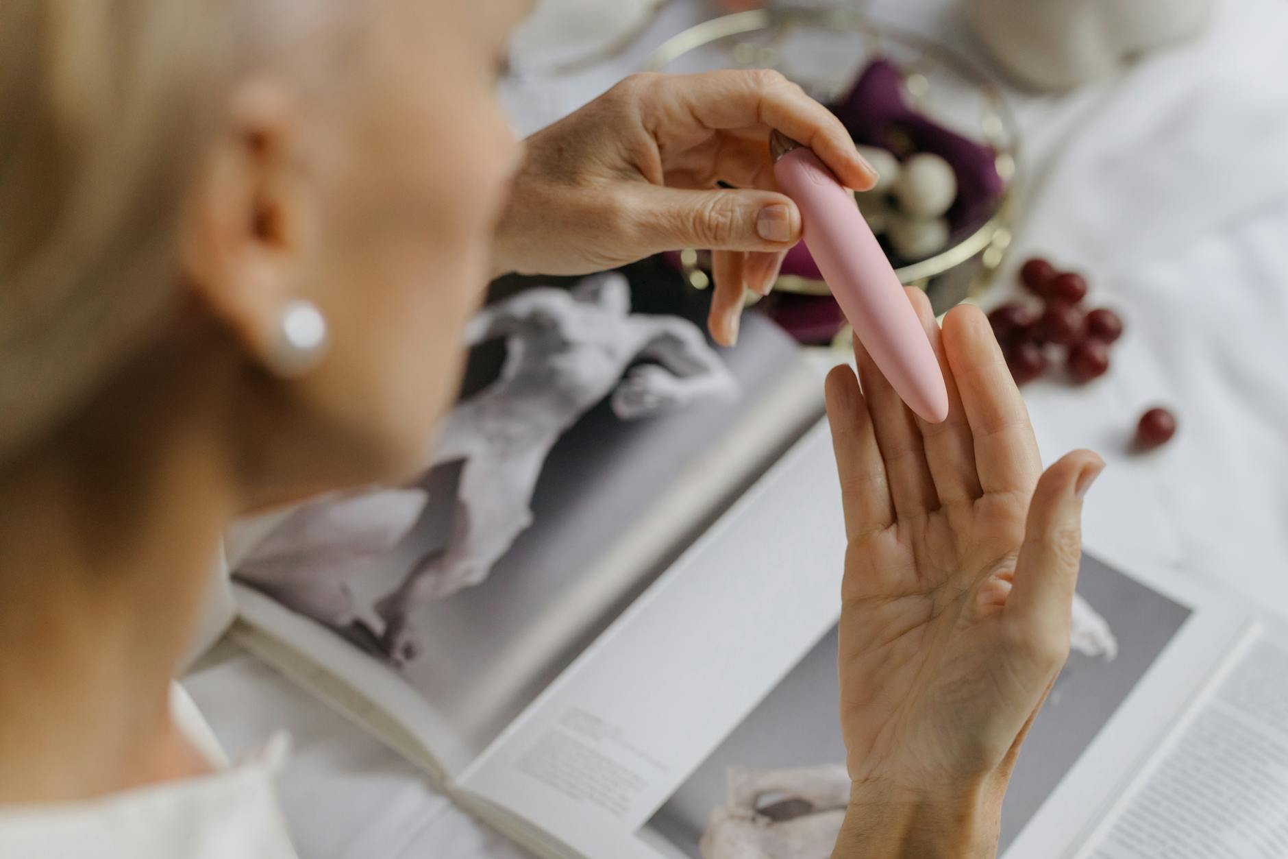 A hand with white nails holding a lemon on a soft pink background, symbolizing personalized touch and precision in intimate moments.
